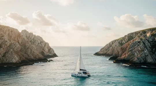 Catamaran voguant seul sur une mer turquoise entre deux caps, symbole du choix éclairé en matière de location de bateau