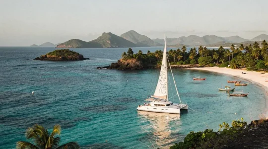 Voilier au mouillage dans une baie turquoise entourée d'ilots verdoyants typique des Grenadines aux Petites Antilles