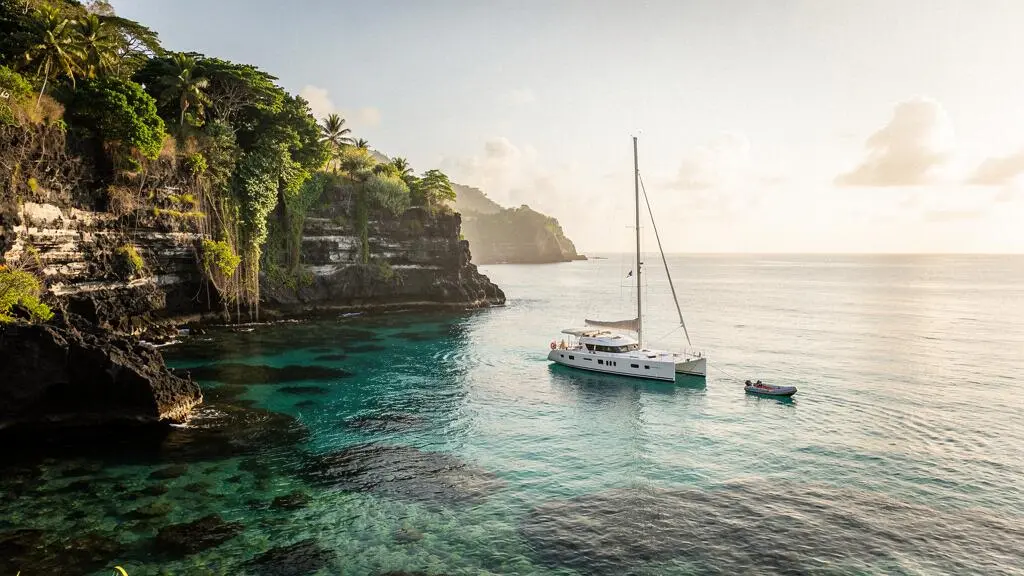 Voilier au mouillage dans une crique sauvage des Antilles aux eaux turquoise, entoure de falaises volcaniques verdoyantes