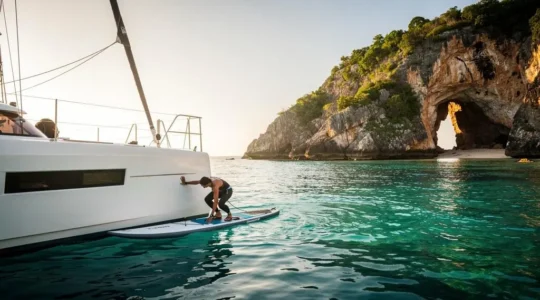 Un stand-up paddle amarré près d'un catamaran ancré au large d'une côte rocheuse tropicale, prêt pour l'exploration