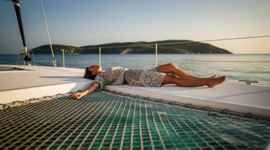 Voyageur détendu allongé sur le trampoline avant d'un catamaran au coucher du soleil, symbole de vacances sans stress