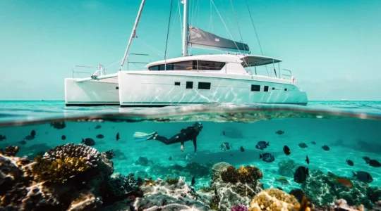 Voilier au mouillage au-dessus d'un lagon turquoise laissant deviner un récif corallien peuplé de poissons tropicaux